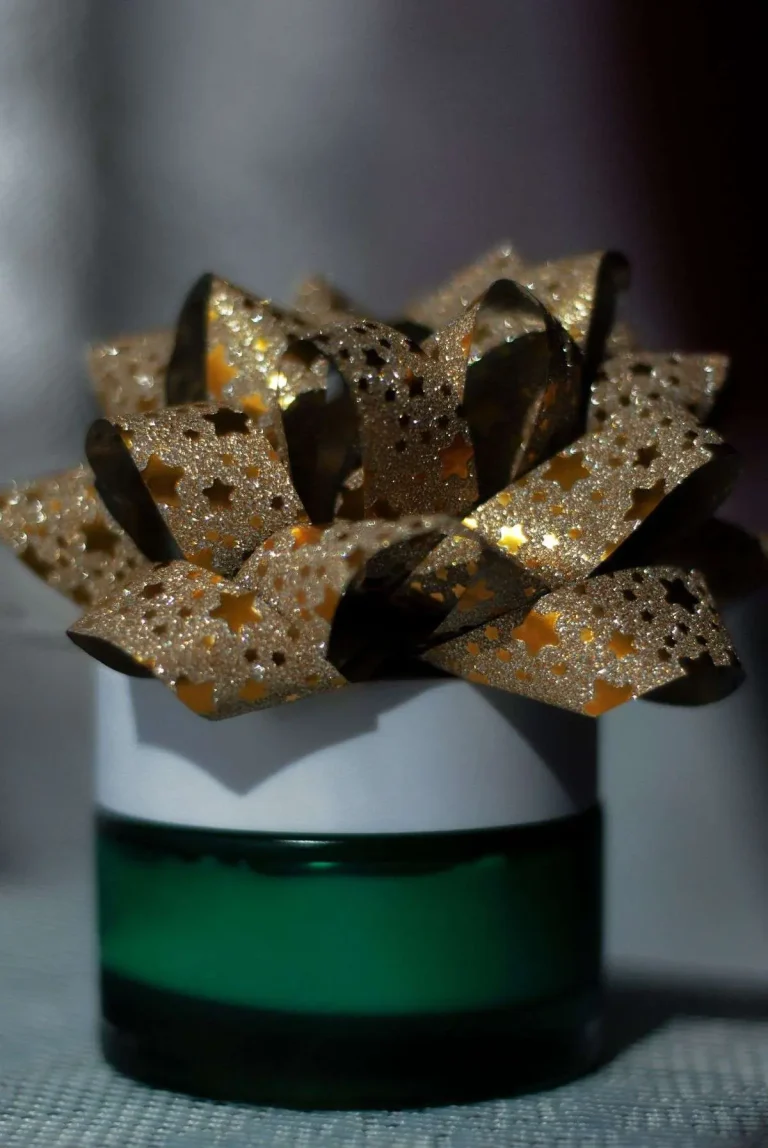 A gold glitter bow with star-shaped cutouts sitting atop a green glass jar