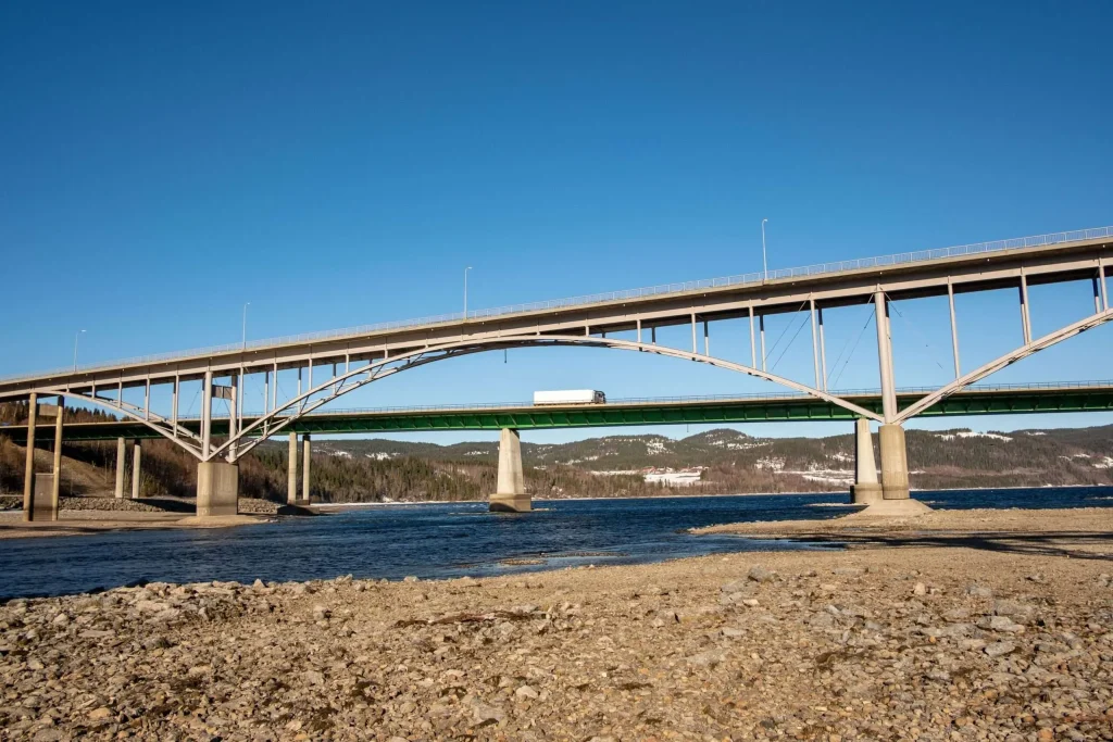 Modern multi-lane highway bridge carrying traffic over a wide river, with forested hills in the background