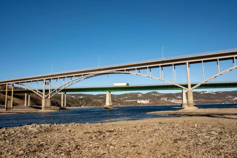 Modern multi-lane highway bridge carrying traffic over a wide river, with forested hills in the background