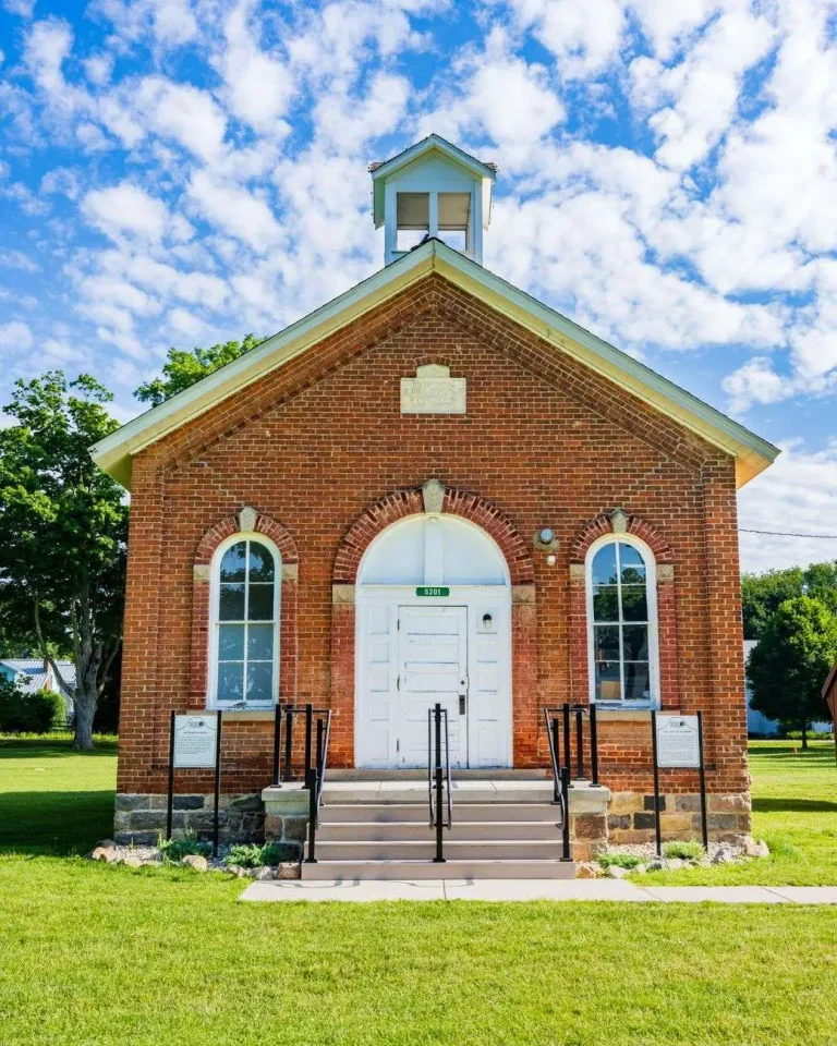 A small historic red brick schoolhouse with a white bell cupola and arched windows