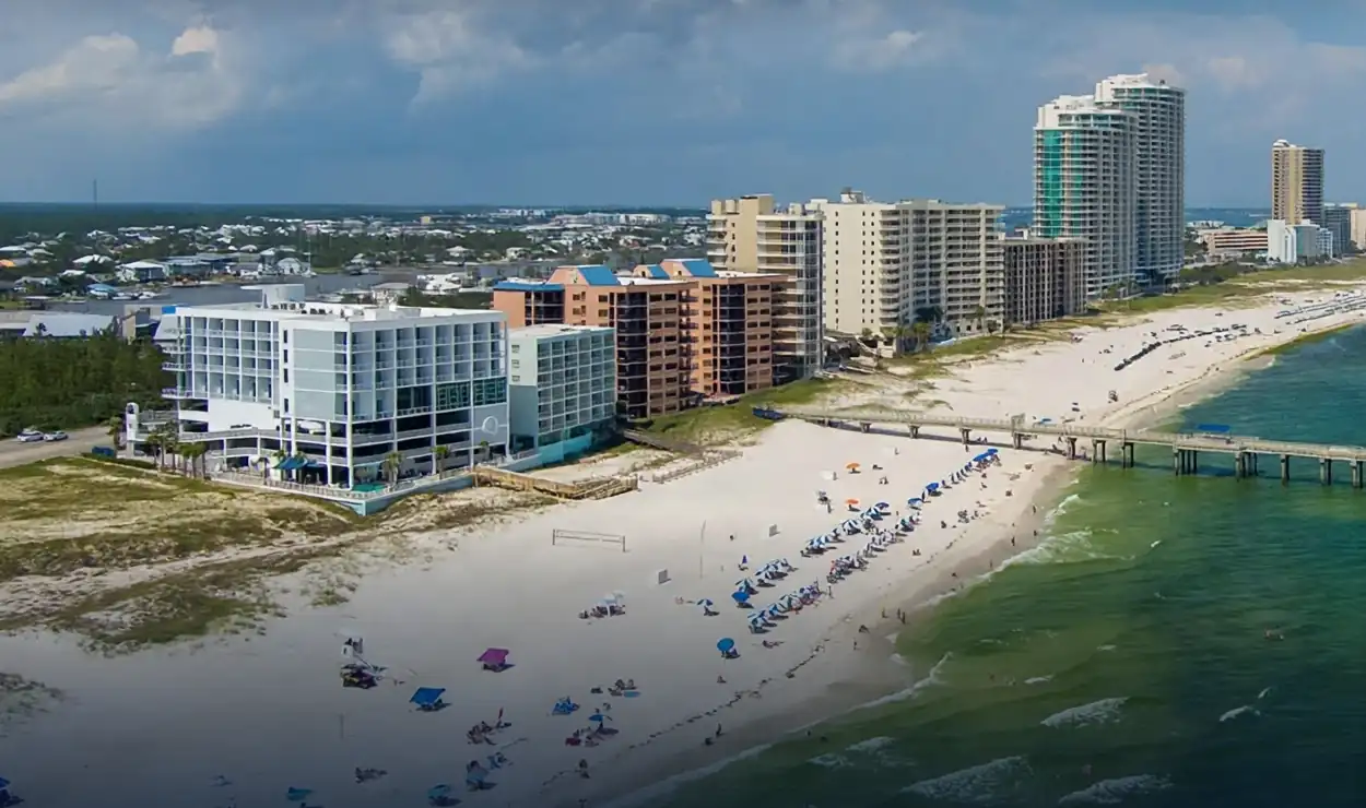 Aerial view of white sand beach, high-rise condominiums and a fishing pier along emerald Gulf water