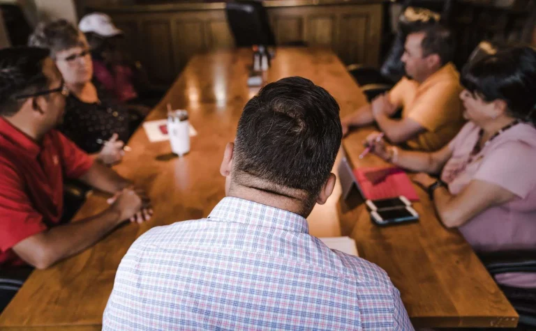 A diverse group of adults seated around a conference table in conversation