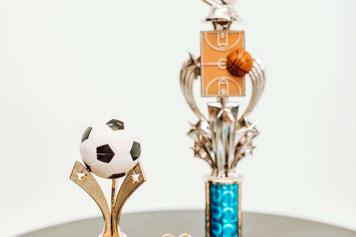 Two sports trophies on a table, one topped with a soccer ball and the other with a basketball charm