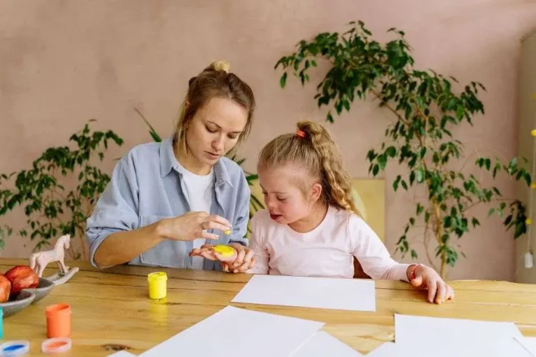 A caregiver reviewing paperwork at a kitchen table with a child nearby