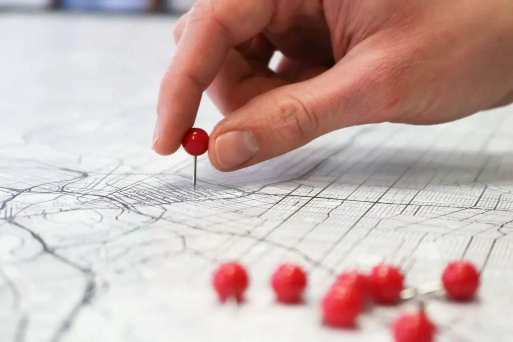 A hand places a red pushpin into a printed street map, with several more pins nearby
