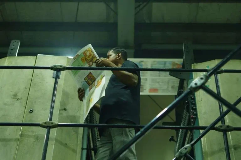 Worker inspects a freshly printed newspaper in an industrial printing press facility