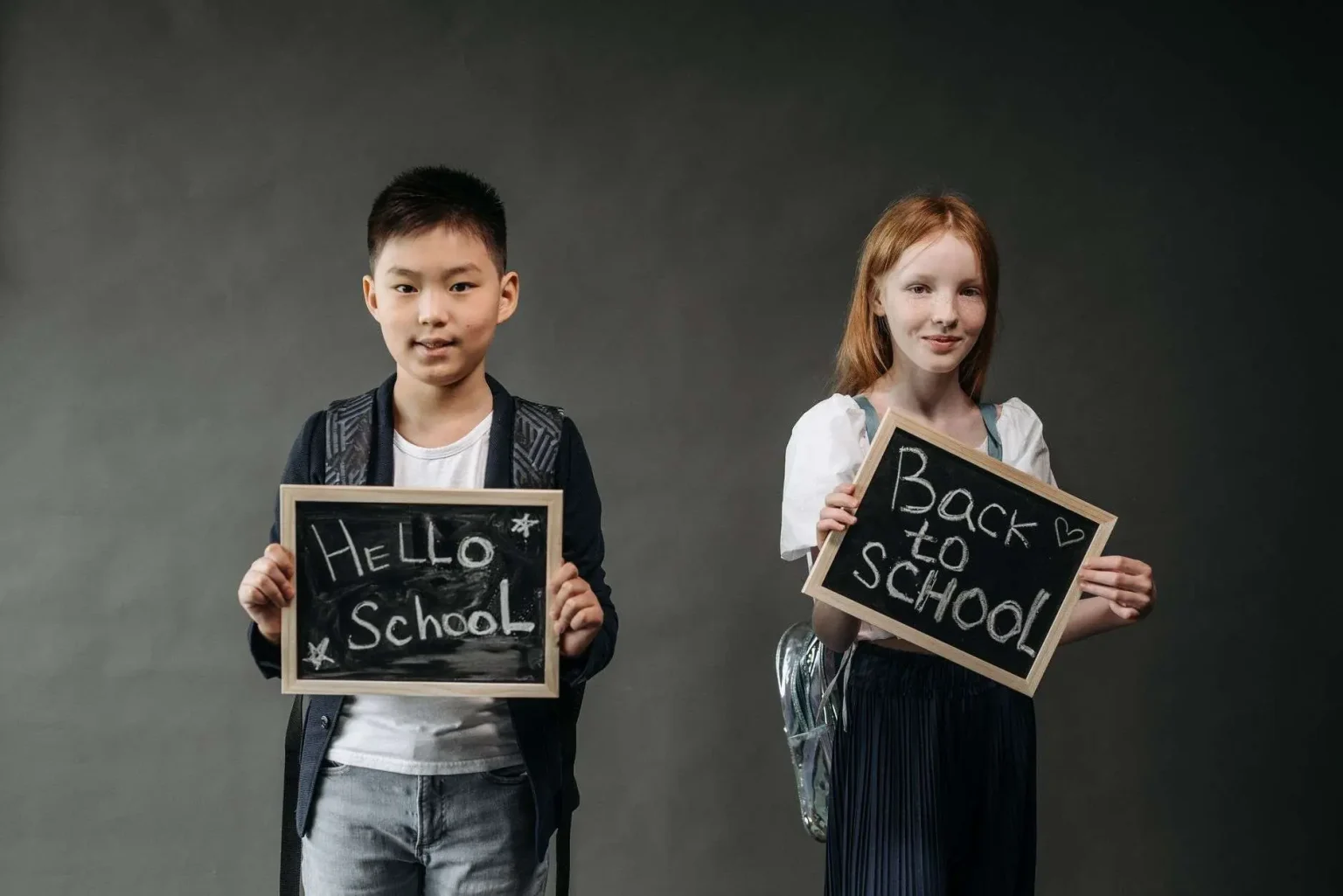 Two children smiling and holding small chalkboard signs reading Hello School and Back to School