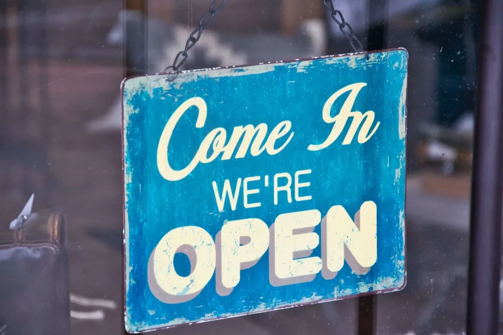 A blue "Come In, We're Open" sign hanging on a shop glass door