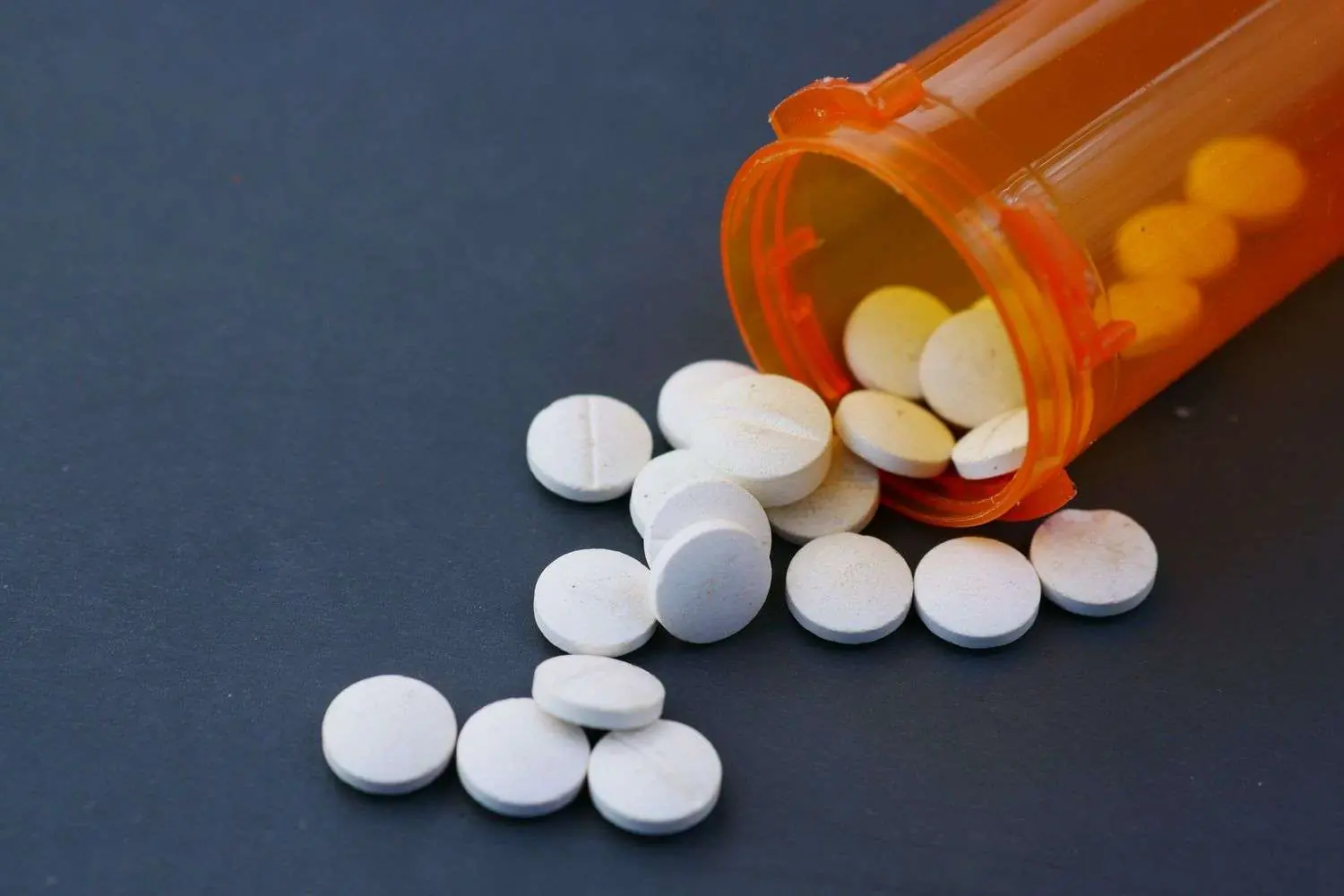 White round tablets spilled out of an open orange prescription pill bottle