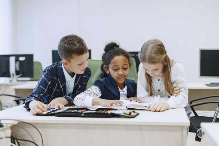 Elementary school students reading a book together at a classroom desk
