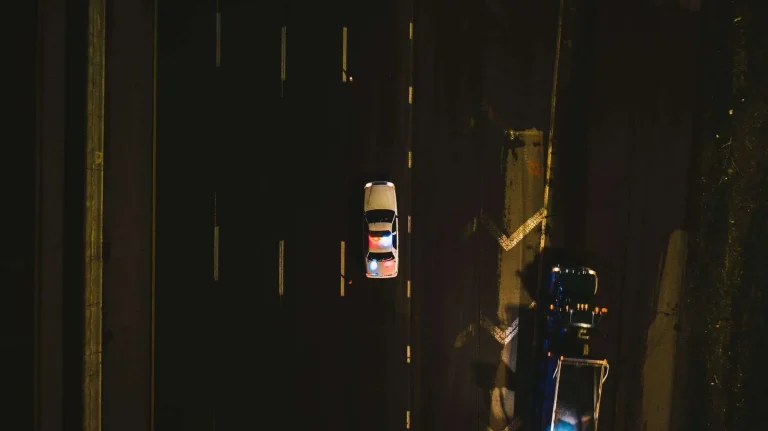 Aerial night view of a police car with red and blue emergency lights activated, driving on a highway behind another vehicle