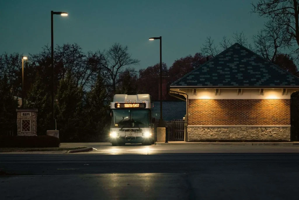 A public transit bus stopped at a curb at night with its headlights and route sign lit