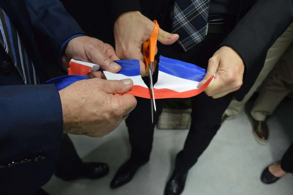 Close-up of hands using scissors to cut a red, white and blue ceremonial ribbon