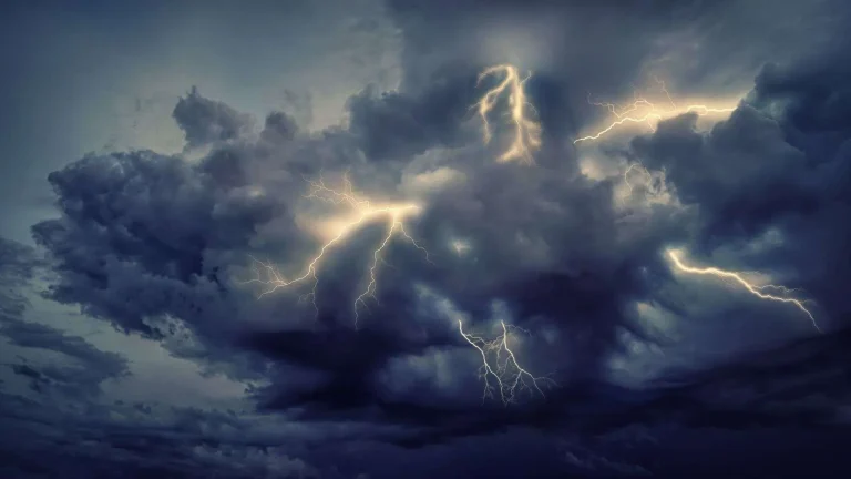 Dark storm clouds lit up by multiple lightning strikes in a night sky