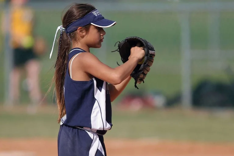 A young softball player in a navy and white uniform holds up her glove while preparing to field or throw on a ball field