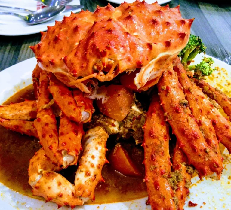 A plate of crab legs in a spiced sauce, garnished with broccoli and tomato