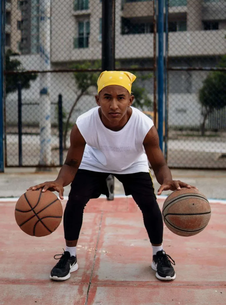 A young man dribbling two basketballs on an outdoor court