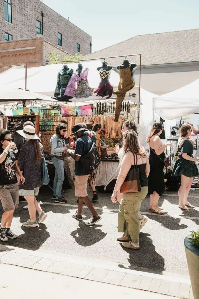 Shoppers browse handmade jewelry, clothing, and craft vendor booths at an outdoor street market.