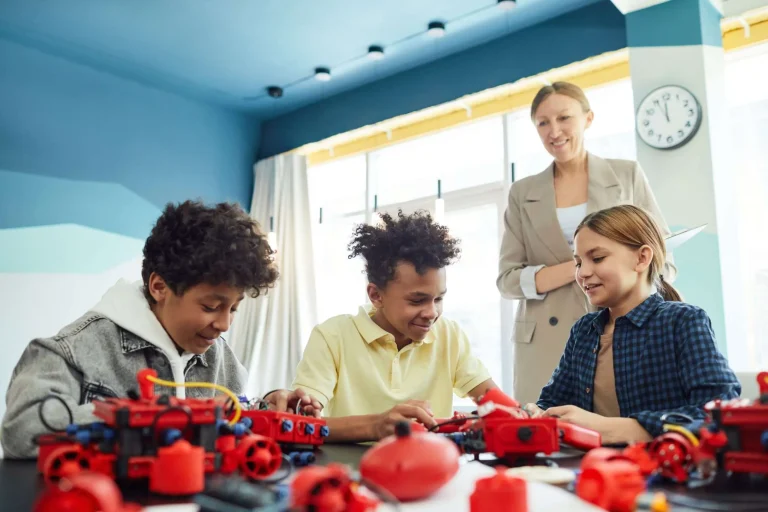 Students working together on a small robotics project at a table while a teacher looks on