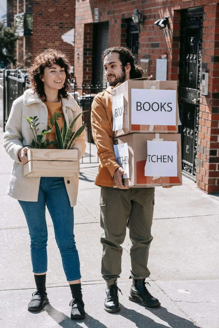 Two young people carrying labeled moving boxes into a building