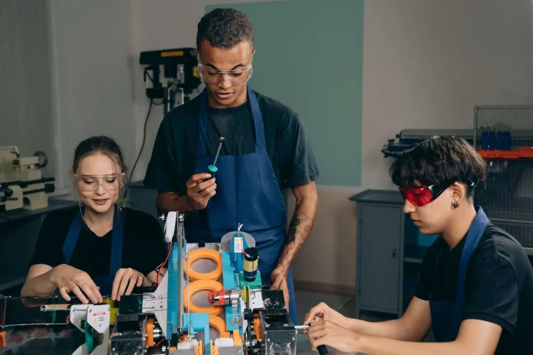 Students wearing safety glasses work together on a mechanical device in a technical training workshop