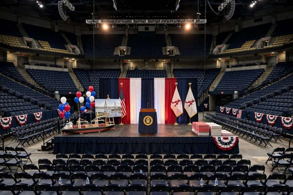 Podium with American flags on a stage inside a crowded college basketball arena lit for an evening political rally