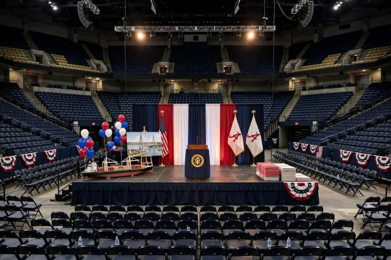 Podium with American flags on a stage inside a crowded college basketball arena lit for an evening political rally