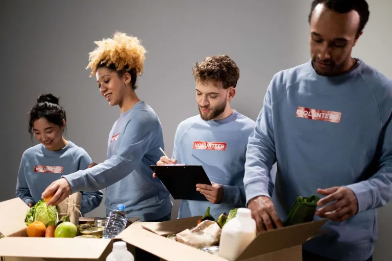 Four volunteers wearing shirts labeled Volunteer pack boxes of fresh produce and groceries