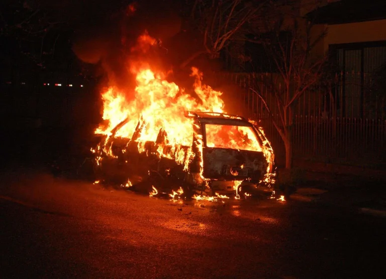 A vehicle fully engulfed in flames at night on a residential street