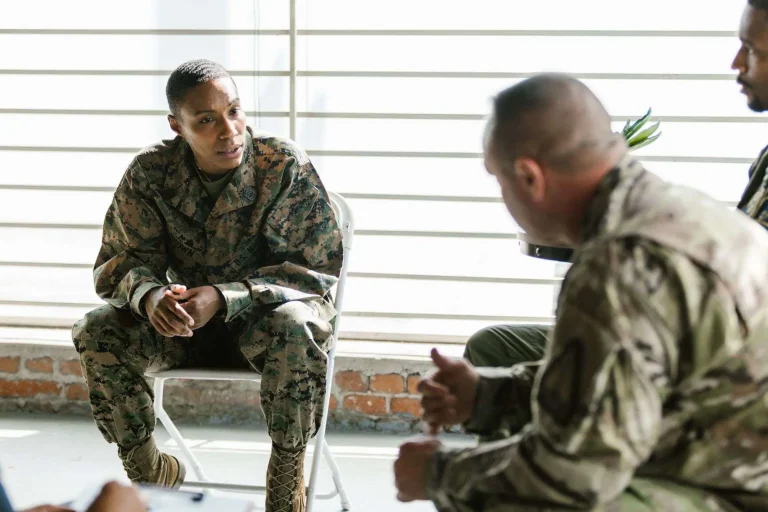 Service members in uniform sit in a circle talking during a group support session.